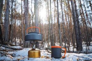 A kettle and a cup are both peacefully resting amidst the thick blanket of snow in the serene woods, surrounded by the stunning beauty of nature and towering trees all around them photo