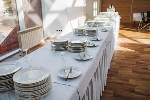 There is a long table beautifully set with plates, glasses, and silverware arranged neatly on it, creating an inviting atmosphere for dining or gathering with friends or family photo