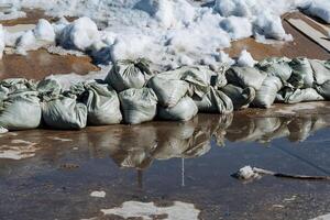 A sizable puddle surrounds several sandbags, which are susceptible to changes in temperature and various weather conditions that occur throughout the different seasons of the year photo