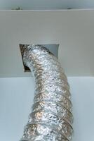 A shiny silver duct is creatively protruding from a small hole in the ceiling above, adding a somewhat intriguing visual element to the otherwise plain and simple structure of the room photo