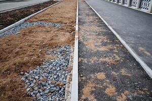Next to a road that is currently under construction, there is a row of dirt and gravel, forming a rough terrain that will eventually support the finished roadway and sidewalks photo