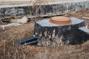 A rusty access cover sits alongside an abandoned pipe in a field characterized by overgrown terrain, evoking feelings of desolation in this historically industrial landscape photo