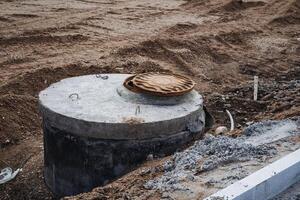 In a typical scenario, a standard manhole cover can be found resting in a dirt field that consists of various elements, including soil, sand, and potentially other building materials photo