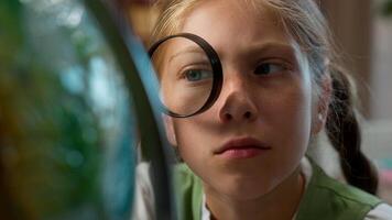 Smart clever curious Caucasian little girl schoolkid child school kid overworked schoolgirl pupil student using magnifying glass looking globe world map research project studying learn indoor library photo