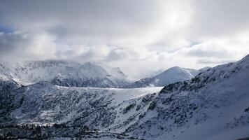 Clouds in the mountains. Majestic winter landscape with snow-capped mountains, densely covered with coniferous forest. photo