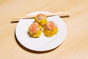 Dimsum and chopsticks on white plate isolated on wooden background. After edits. photo