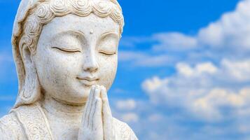 Serene White Buddha Statue with Closed Eyes and Praying Hands Against Blue Sky with Clouds photo