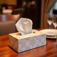 A tissue box sitting on a table with a plate and wine glasses photo