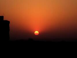 The sun setting over a tower in the distance photo