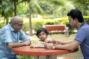 Wise Old Man Playing Chess With Grandson And Son photo