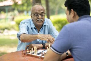 Smiling Old Man Playing Chess On Table In Park With Son photo