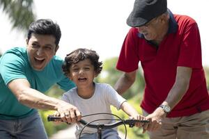 Innocent Boy Learning Bicycle With Assistance Of Father And Grandfather At Park photo