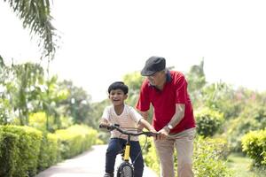 Happy Grandpa Trying To Teach Grandson To Ride A Cycle At Park photo