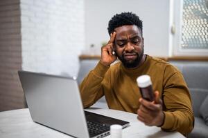 African American man using a computer to search for health advice and possible solutions to a medical issue, showing signs of pain and uncertainty while reviewing options. photo