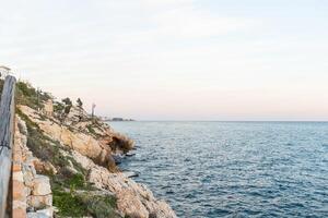 A rocky coastal path leading to the sparkling blue Mediterranean Sea under bright summer sun, clear skies and calm waves. photo