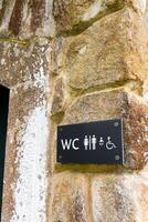 A signage points to the public toilet and includes a symbol for disable person. Clear icons of a man, woman, and wheelchair on yellow design background with a black arrow indicating the direction. photo