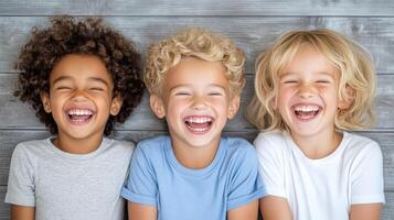 Three children laughing and smiling in front of a wooden wall photo