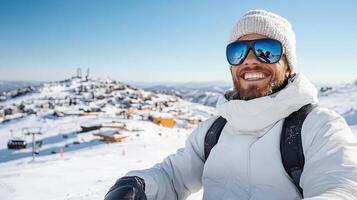 A man in a white coat and ski goggles smiles while standing on a snowy mountain photo