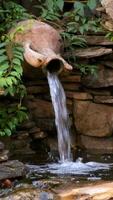 A small decorative mushroom fountain in a stone pool with a waterfall from a pitcher. Landscape design. video