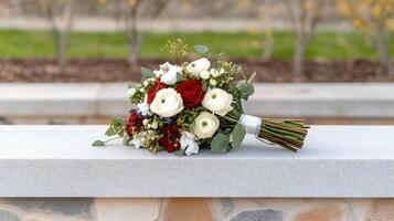 A bouquet of red and white flowers sitting on a stone ledge photo