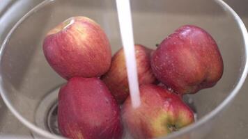 Red apples being washed in clear glass bowl under stream of water video
