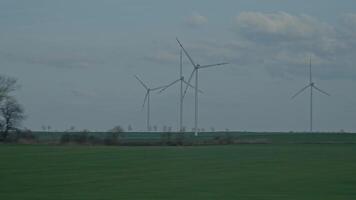 Wind turbines spin across a green field, filmed from a moving vehicle. Renewable energy and clean power video