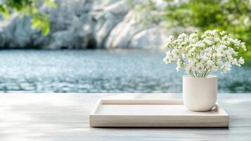 White flowers in a vase on a wooden tray near a lake photo