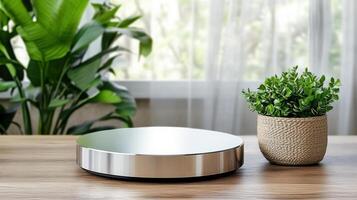 A silver circular device sits on a table next to a plant photo