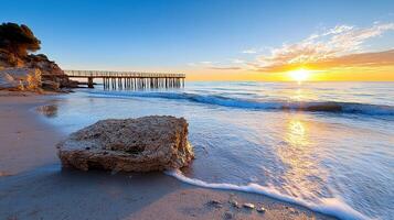 A beach with a pier and rocks at sunset photo