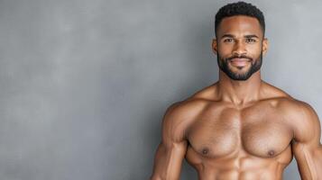 A man with no shirt on standing in front of a gray wall photo
