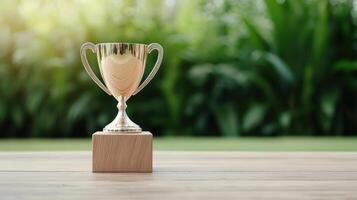 Golden trophy cup on wooden table in front of green grass background photo