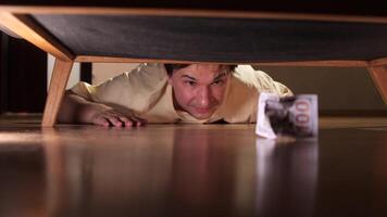 Man crawling on floor searching for lost money under furniture video