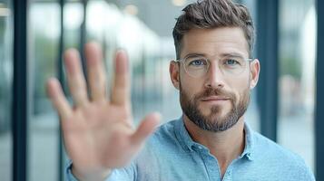 A man with glasses and a beard is holding up his hand photo
