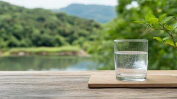A glass of water on a wooden table with a lake in the background photo