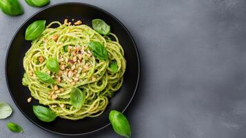 Spaghetti with pesto and basil leaves on a black plate photo