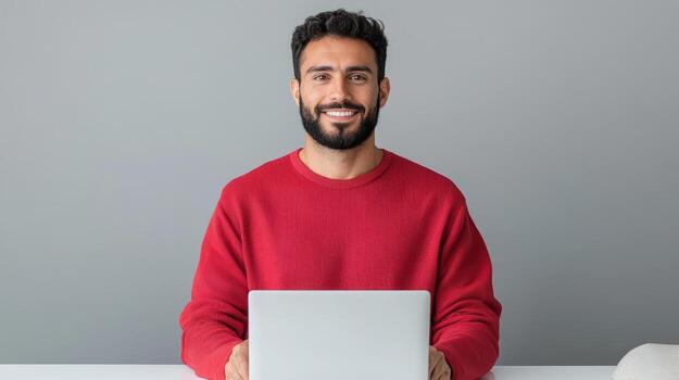 A man in a red sweater is sitting at a table with a laptop photo