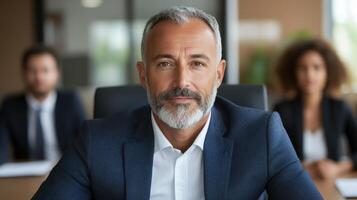 A man with a beard and a suit is sitting in front of a group of people photo