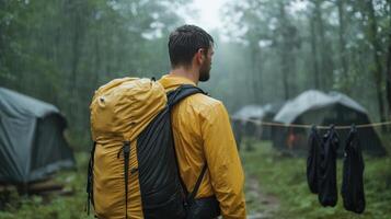 Man with yellow rain jacket and backpack walking through campground photo