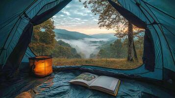 serene camping scene inside tent showcases beautiful view of mountains and misty valleys at sunrise. book lies open beside lantern, inviting relaxation and connection with nature photo