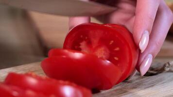 Close-up of hand slicing fresh red tomato with a sharp knife on wooden board, focusing on food preparation, vibrant color, and healthy cooking in kitchen setting video