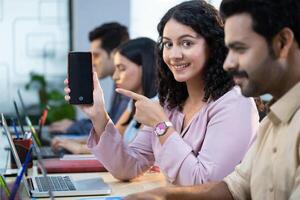 Female Employee Female Sitting On Office Desk Pointing On Mobile Phone Screen photo