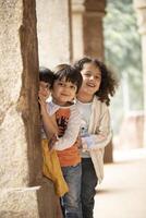Little Children Posing In Front Of Camera While Standing Behind Ancient Column photo