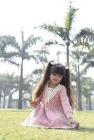 Curious Girl Holding Magnifying Glass While Sitting On Grass photo