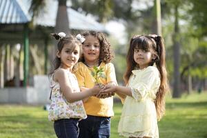 Three Kids Holding In Hands Plant While Posing In Front Of Camera photo