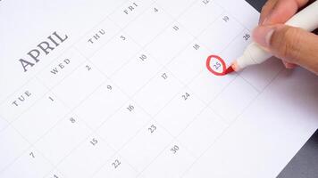Red circle marked on a calendar at 25 of April isolated on black background for an important day photo