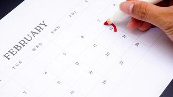 Hand holding marker to make mark on calendar at 14 of February as symbol of valentine day isolated on black background photo