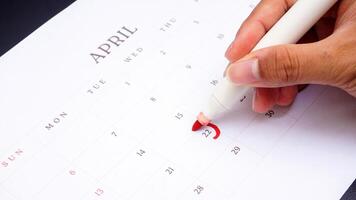 Hand holding marker to make mark on calendar at 22 of April as symbol of important day isolated on black background photo