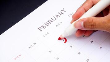 Hand holding marker to make mark on calendar at 4 of February as symbol of important day isolated on black background photo