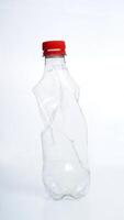 Empty crumpled plastic bottle with red bottle cap isolated on white background photo