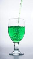 Green colored water poured into drinking glass isolated on white background photo
